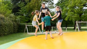 A group of people on a yellow outdoor play area with trees in the background.