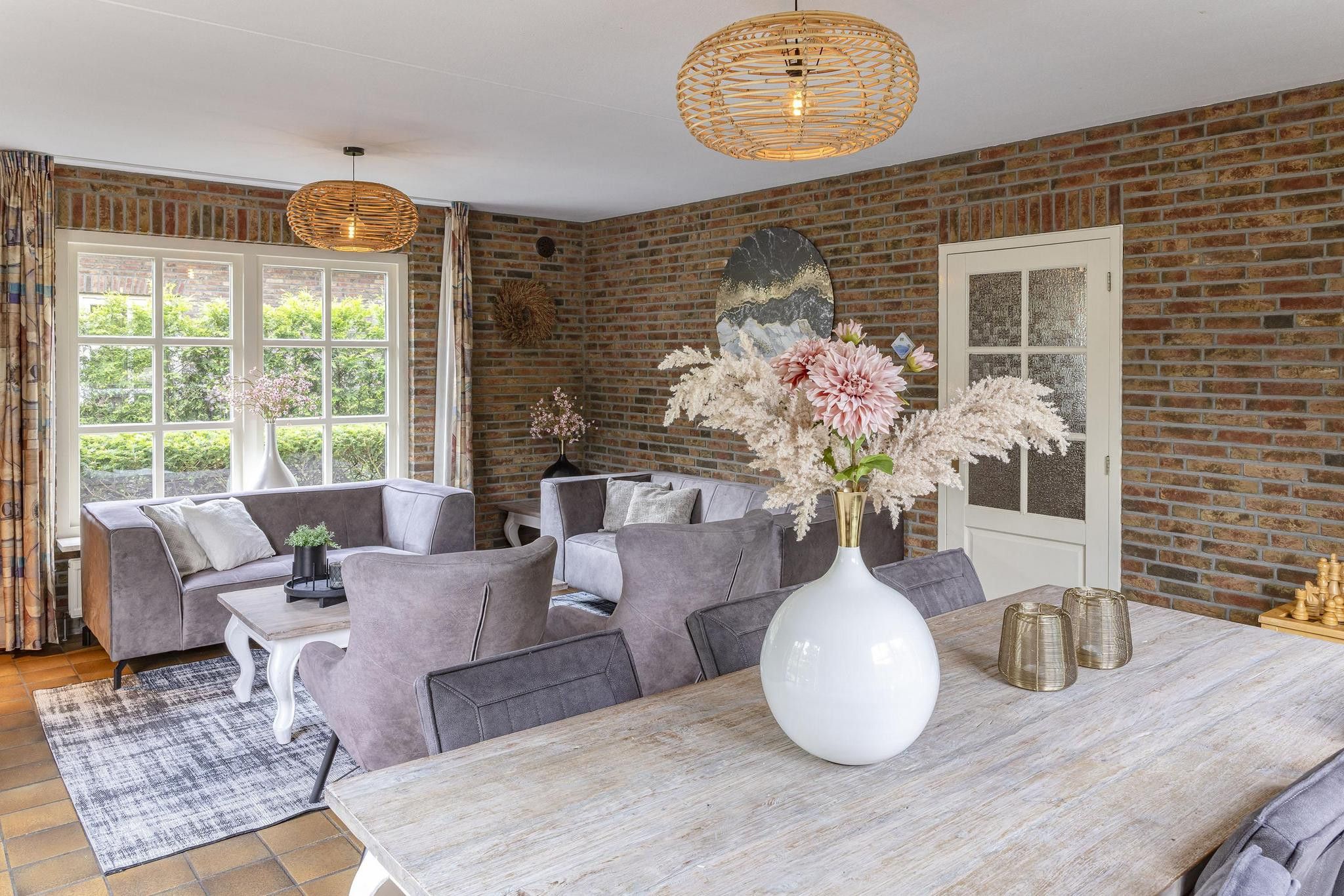A room with a brick wall, a large window, a dining table with chairs, and a sofa.
