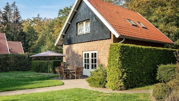 Een tweelaags huis met een rode dakbedekking, een bakstenen gevel en een verzorgde tuin met een patio tafel en stoelen.