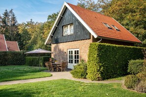 A two-story house with a red-tiled roof, a brick facade, and a well-maintained garden with a patio table and chairs.