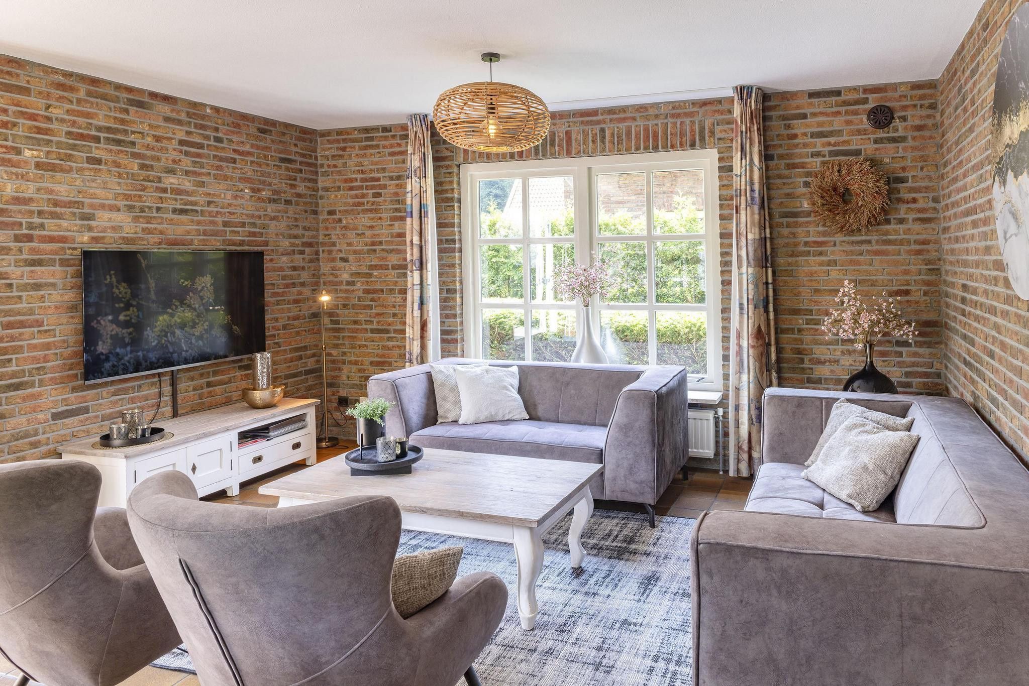 A living room with a brick wall, a television, a sofa, a coffee table, and a window with curtains.