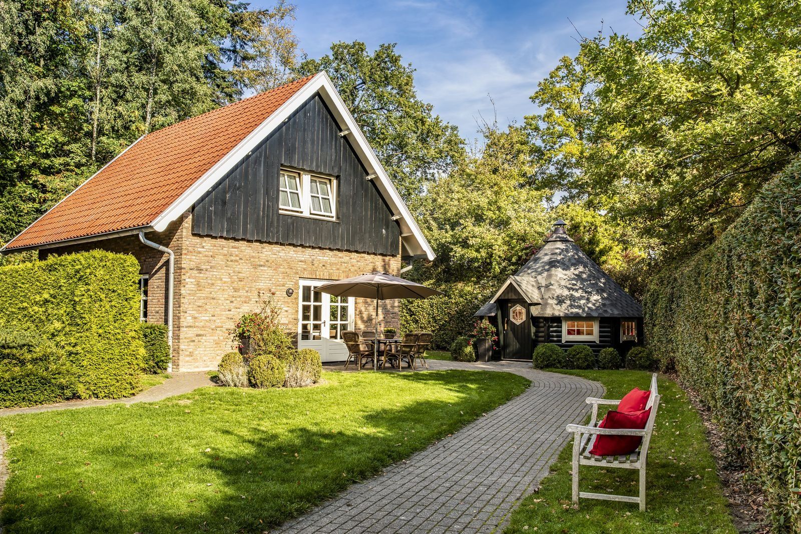 A house with a brick exterior, a red-tiled roof, and a small attached structure with a conical roof.