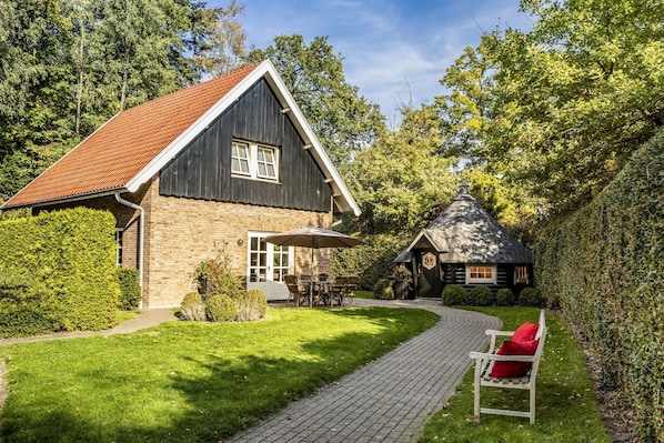 A house with a brick exterior, a red-tiled roof, and a small attached structure with a conical roof.