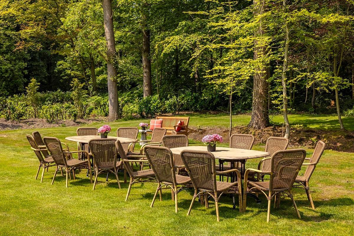 Een buitenterras met rieten meubilair en een tafel, omringd door weelderige begroeiing en bomen.