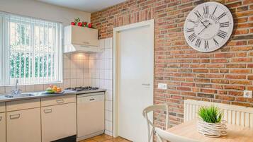 A kitchen with a brick wall, a clock, and a dining area with a plant.