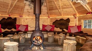 A log fire stove in a wooden cabin with fur rugs and pillows.