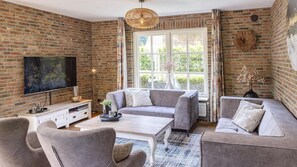 Un salon avec un mur en briques, une grande fenêtre et un téléviseur à écran plat.