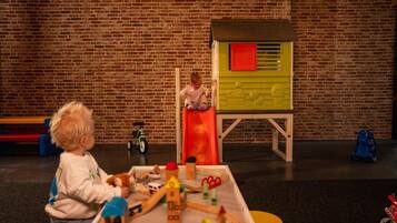 A child playing with toys in a room with a brick wall and a playhouse.