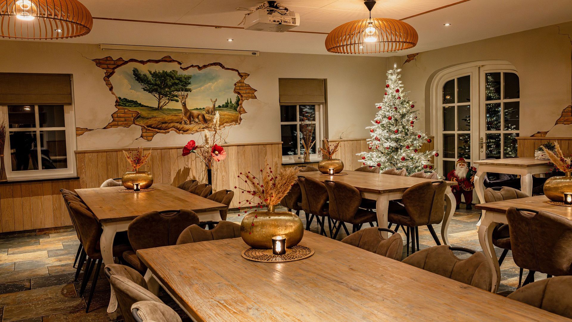 Een eetgedeelte met houten tafels en stoelen, een muurschildering en een kerstboom.
