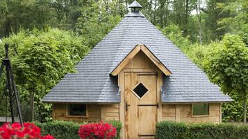 A small wooden structure with a steeply pitched roof, a door with a diamond-shaped window, and a small triangular roof ornament.