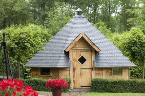 Ein kleines Holzgebäude mit einem steilen Satteldach, einer Tür mit einem rautenförmigen Fenster und einem kleinen dreieckigen Dachzierstück.