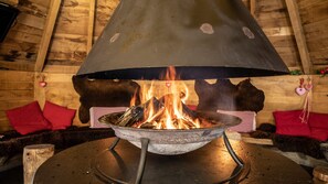 Un foc de llenya amb una campana metàl·lica, envoltat de parets de fusta i coixins vermells.