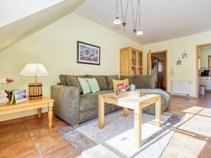 Ein gemütliches Wohnzimmer mit einer Couch, einem Couchtisch und einer Lampe. An der Wand hängt ein gerahmtes Bild, und eine Tür führt in einen anderen Raum.