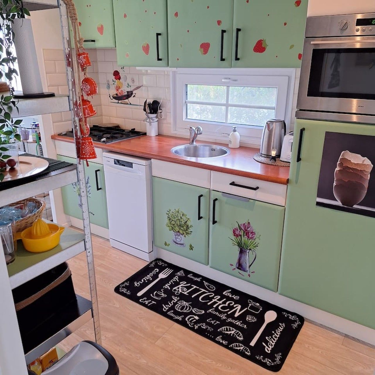 Une cuisine avec des meubles de couleur verte, un four en acier inoxydable, une fenêtre et un tapis de cuisine noir avec du texte blanc.