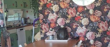 Un comedor con mesa y sillas de madera, un papel tapiz floral y un espejo redondo en la pared.