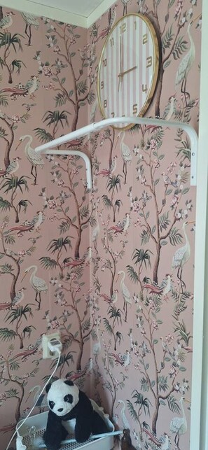 Ein Zimmer mit blumigem Tapetenmuster, einer Uhr und einem Panda-Plüschtier.