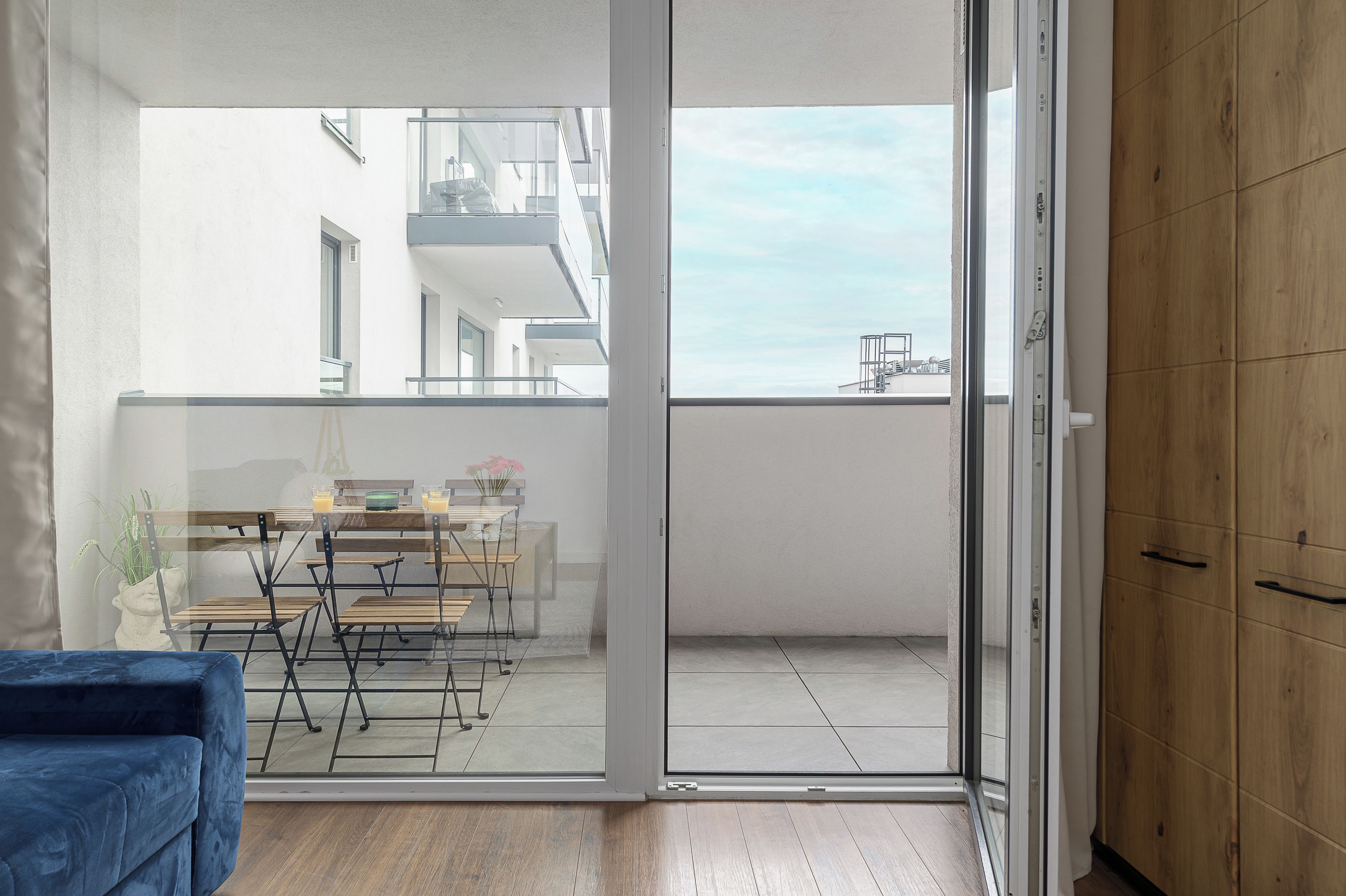 Ein Balkon mit Tisch und Stühlen, ein blaues Sofa und ein Holzschrank.