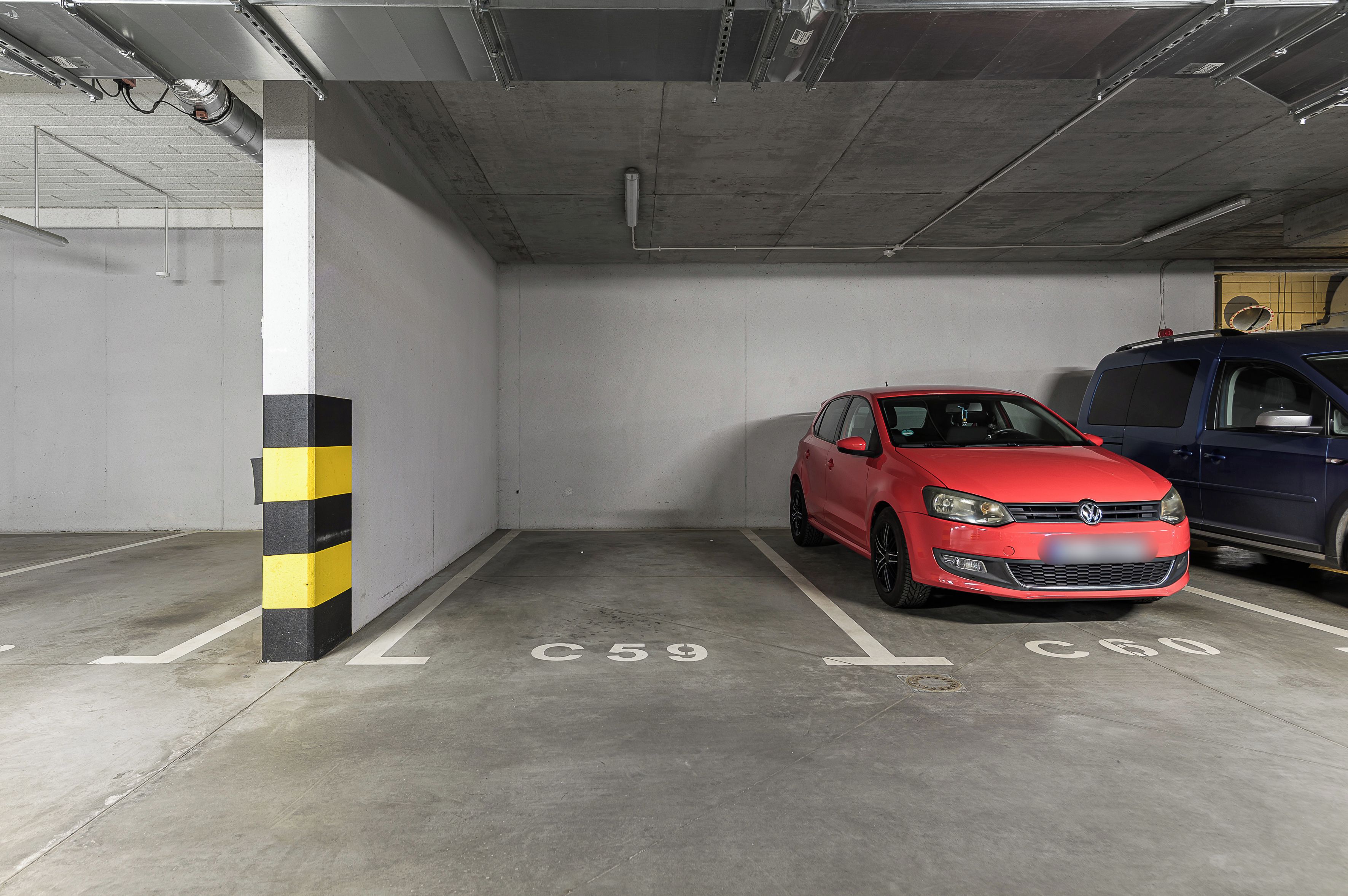 A parking garage with concrete floors and walls, marked parking spaces, and a red car parked in one of the spaces.