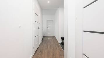 A narrow hallway with white walls and wooden flooring, leading to a door at the end.