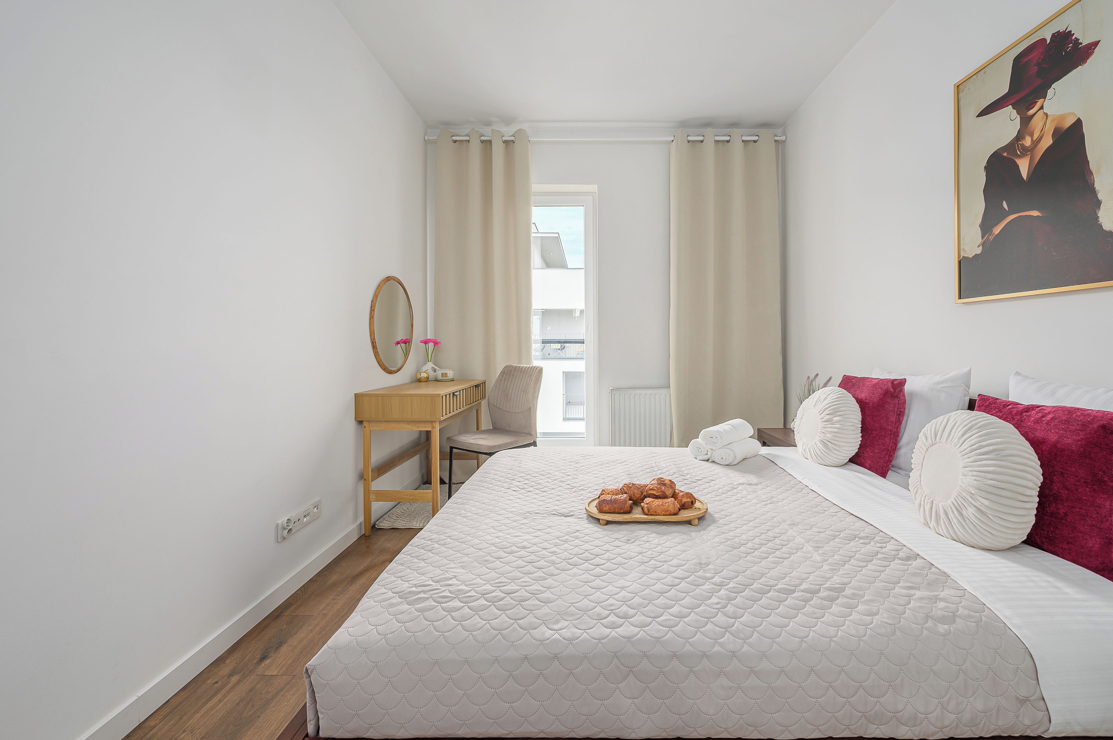 Een slaapkamer met een bed, een bureau, een stoel, een raam en een schilderij aan de muur.