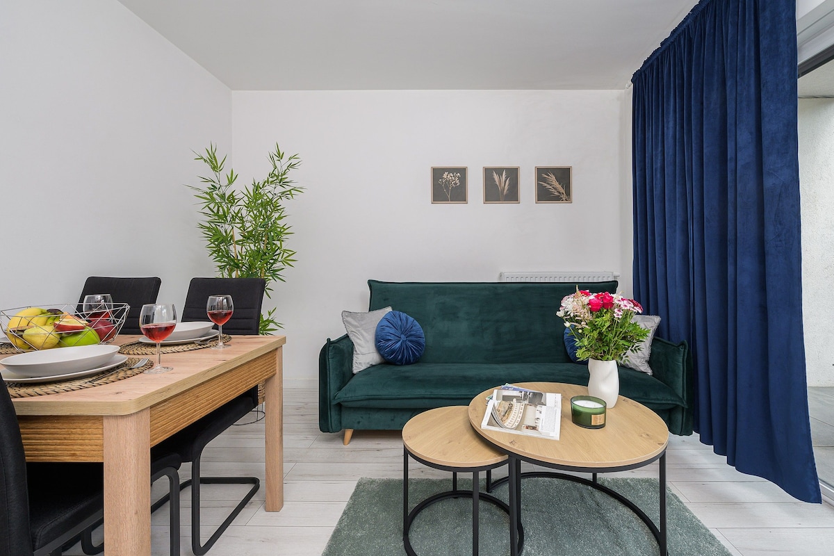 A modern living space with a dining area, a green sofa, a small round table, and a potted plant.