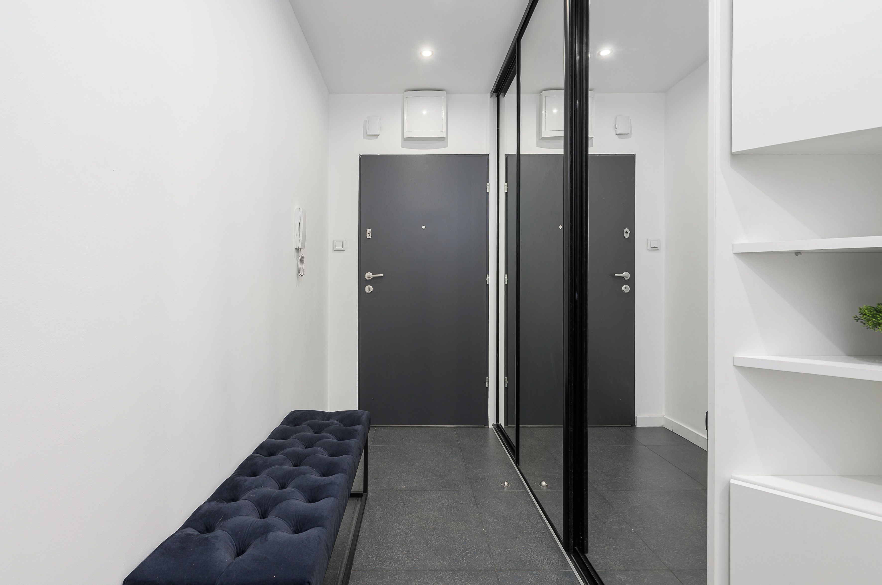 A hallway with a bench, a set of doors, and a white shelf unit.