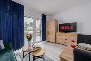 Una sala moderna con un televisor mostrando 'NETFLIX', un mueble de madera, una mesita con una revista y un sofá.