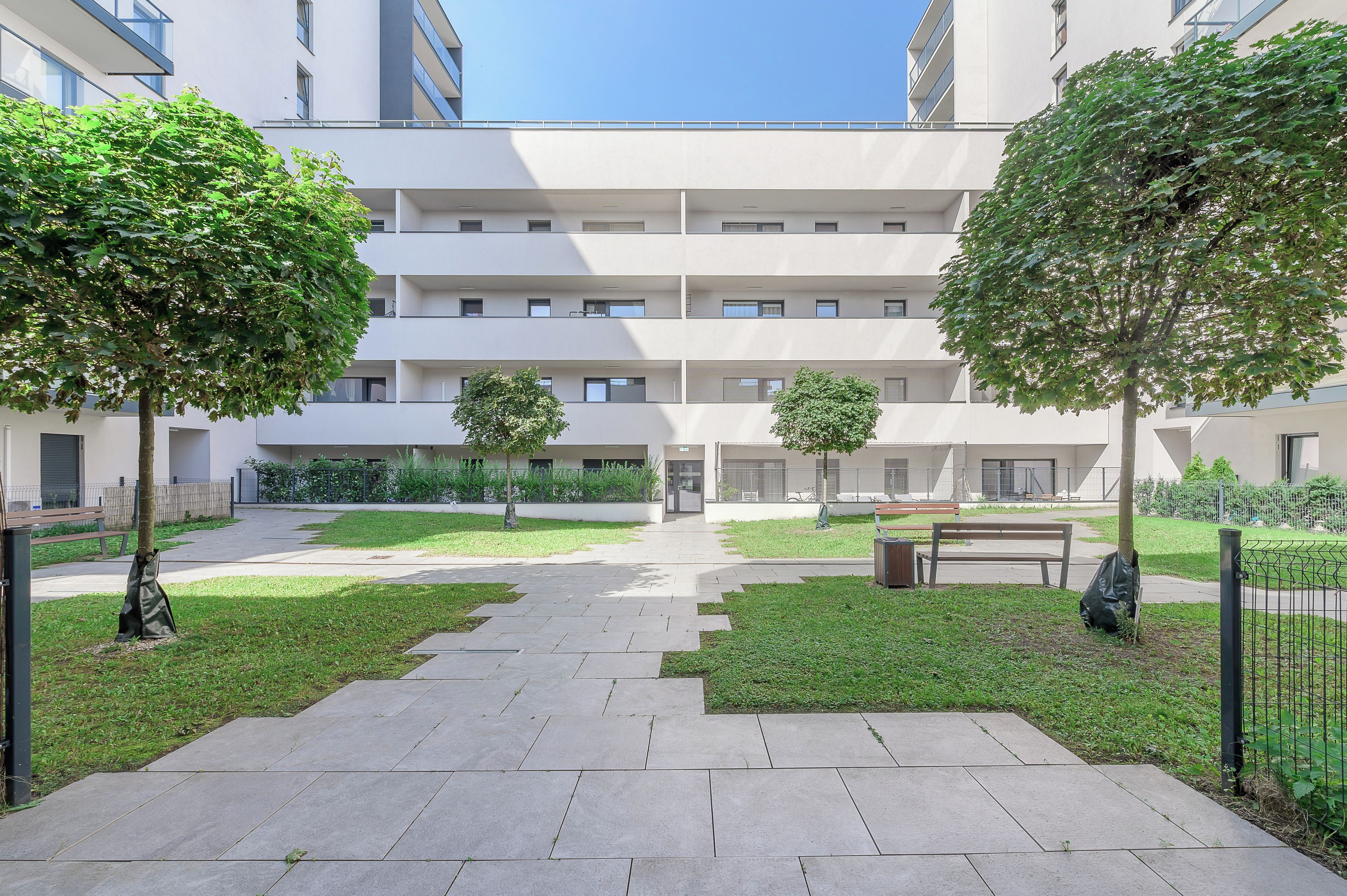 A courtyard with a central pathway, surrounded by greenery and benches.