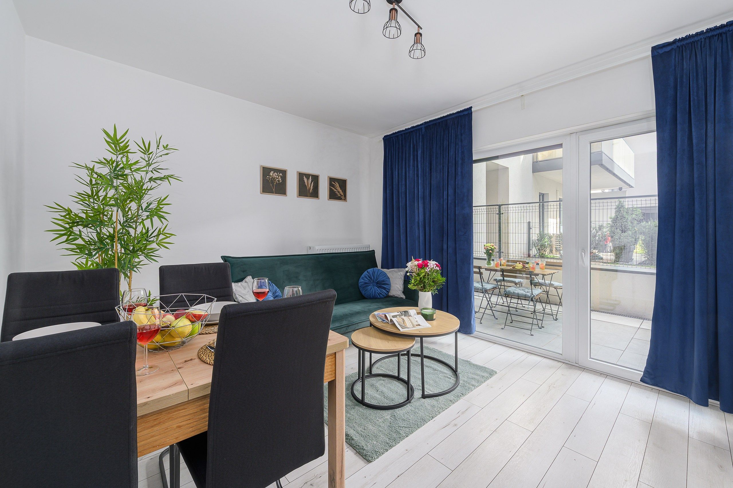 Una sala de estar moderna con comedor, un sofá verde, una mesa de comedor con sillas, una planta en maceta y vistas a través de un ventanal.