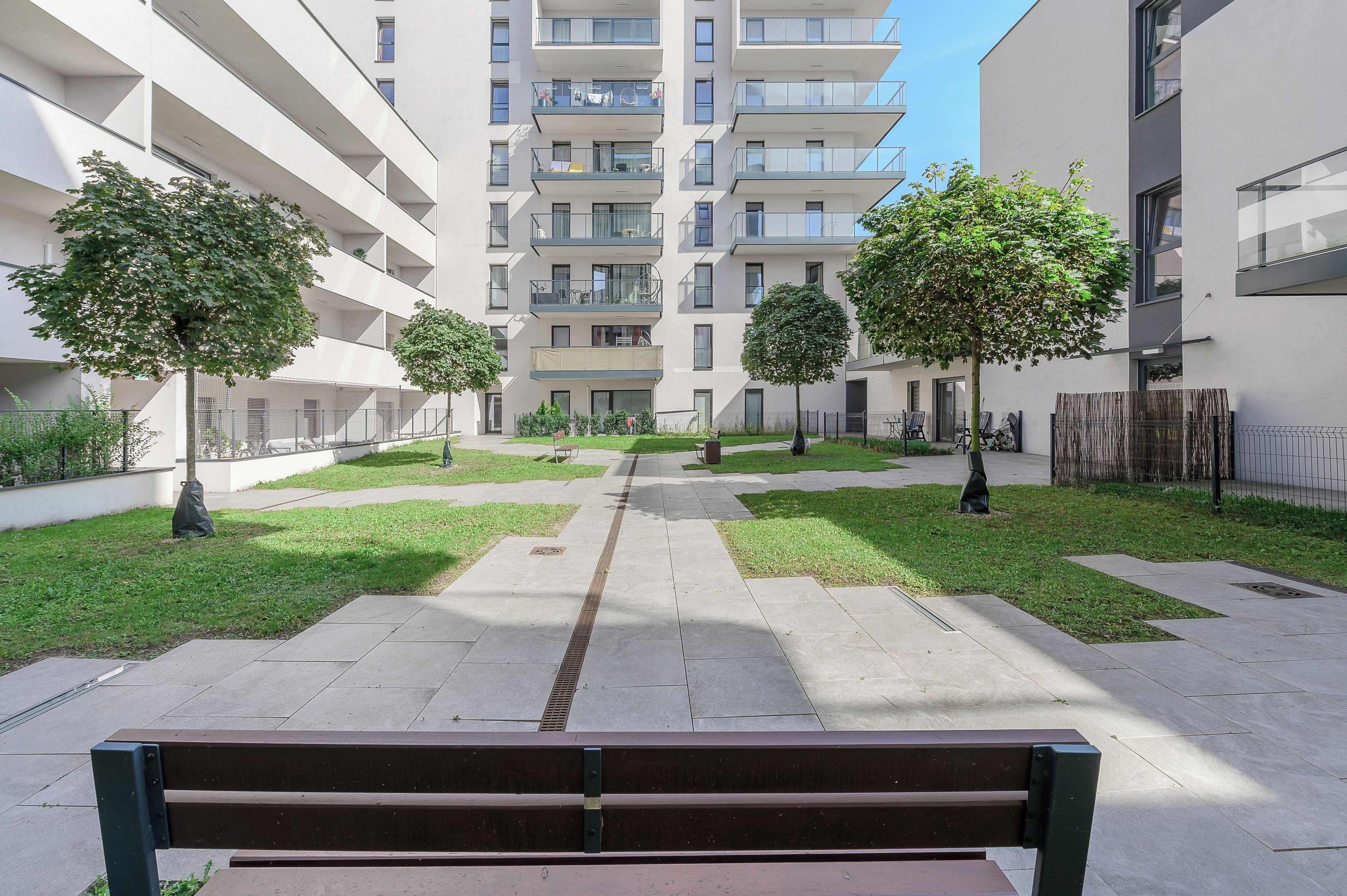 A courtyard with a bench, trees, and a multi-story building with balconies.