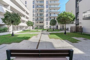 A courtyard with a bench, trees, and a multi-story building with balconies. - Lumina 3room Apt w/ Parking  (Łódź)