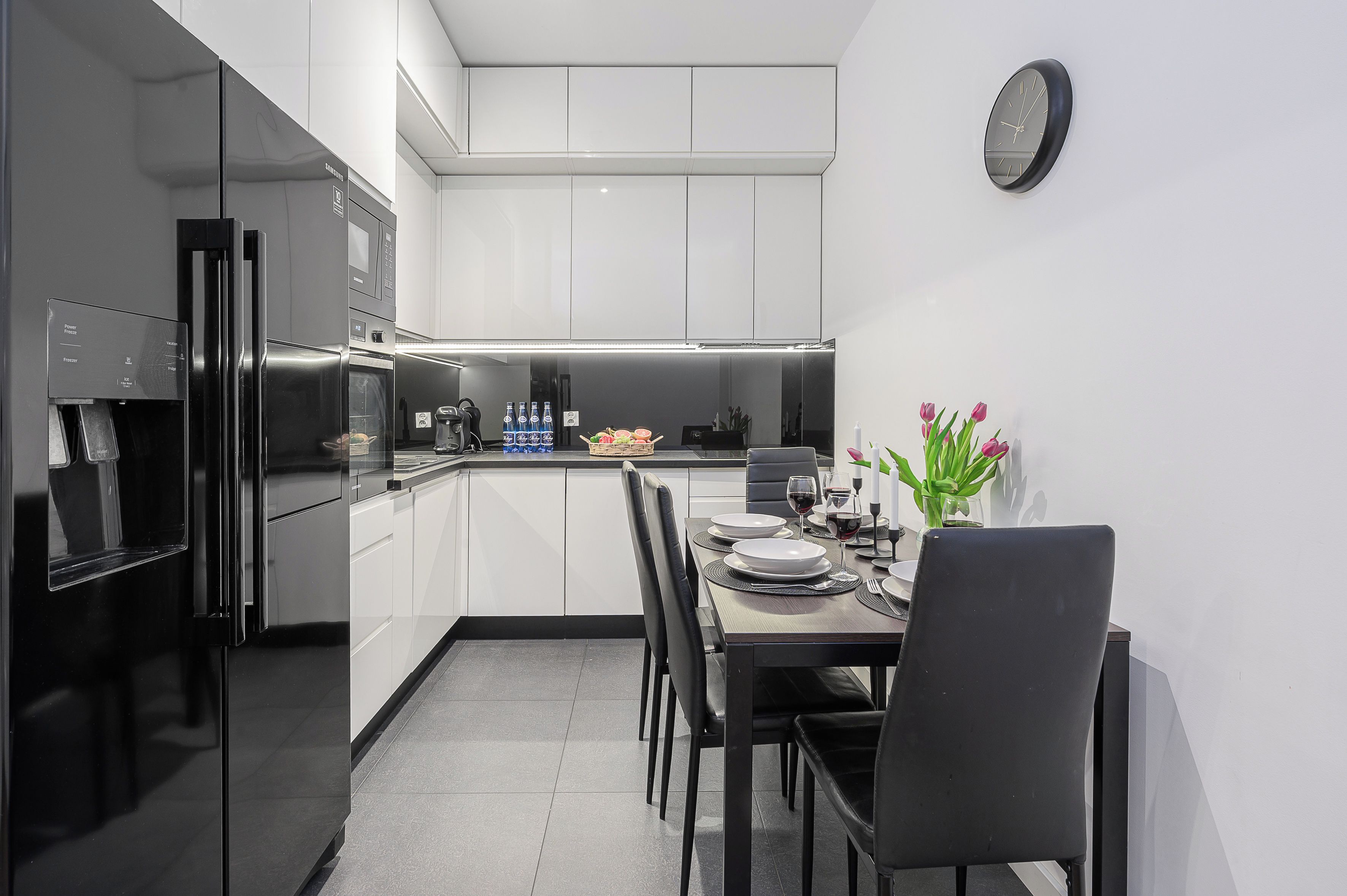 A modern kitchen with white cabinets, a dining table set for four, and a clock on the wall.