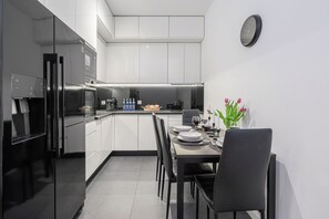 A modern kitchen with white cabinets, a dining table set for four, and a clock on the wall. - Lumina 3room Apt w/ Parking  (Łódź)