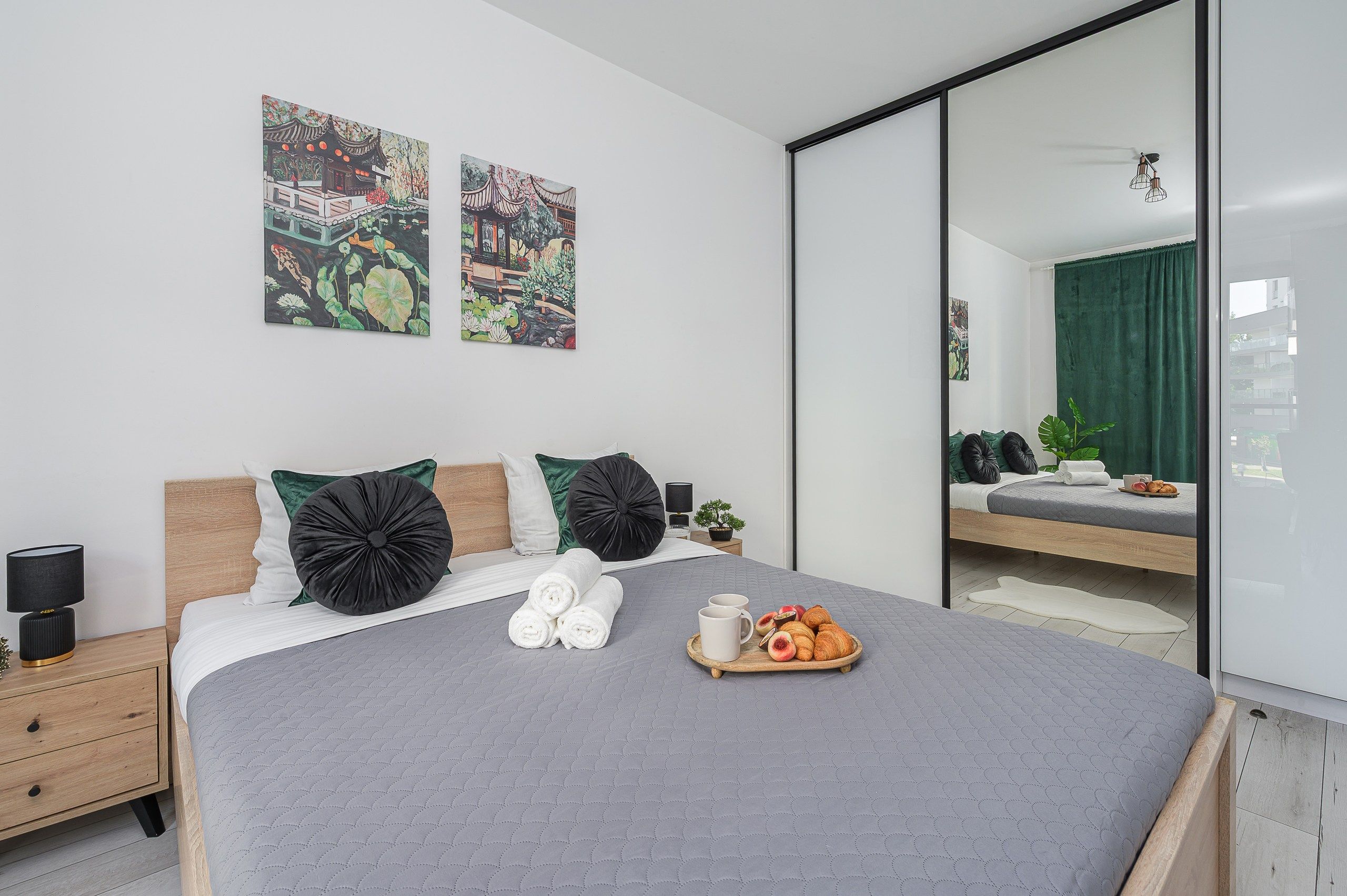 Une chambre à coucher moderne avec un lit, des oreillers, une table de chevet, une commode, un miroir et des œuvres d’art accrochées au mur.