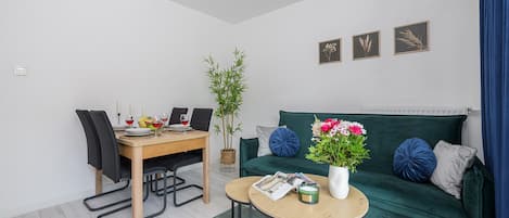 A modern living room with a dining area, a green sofa with decorative pillows, a small round table, and a potted plant.