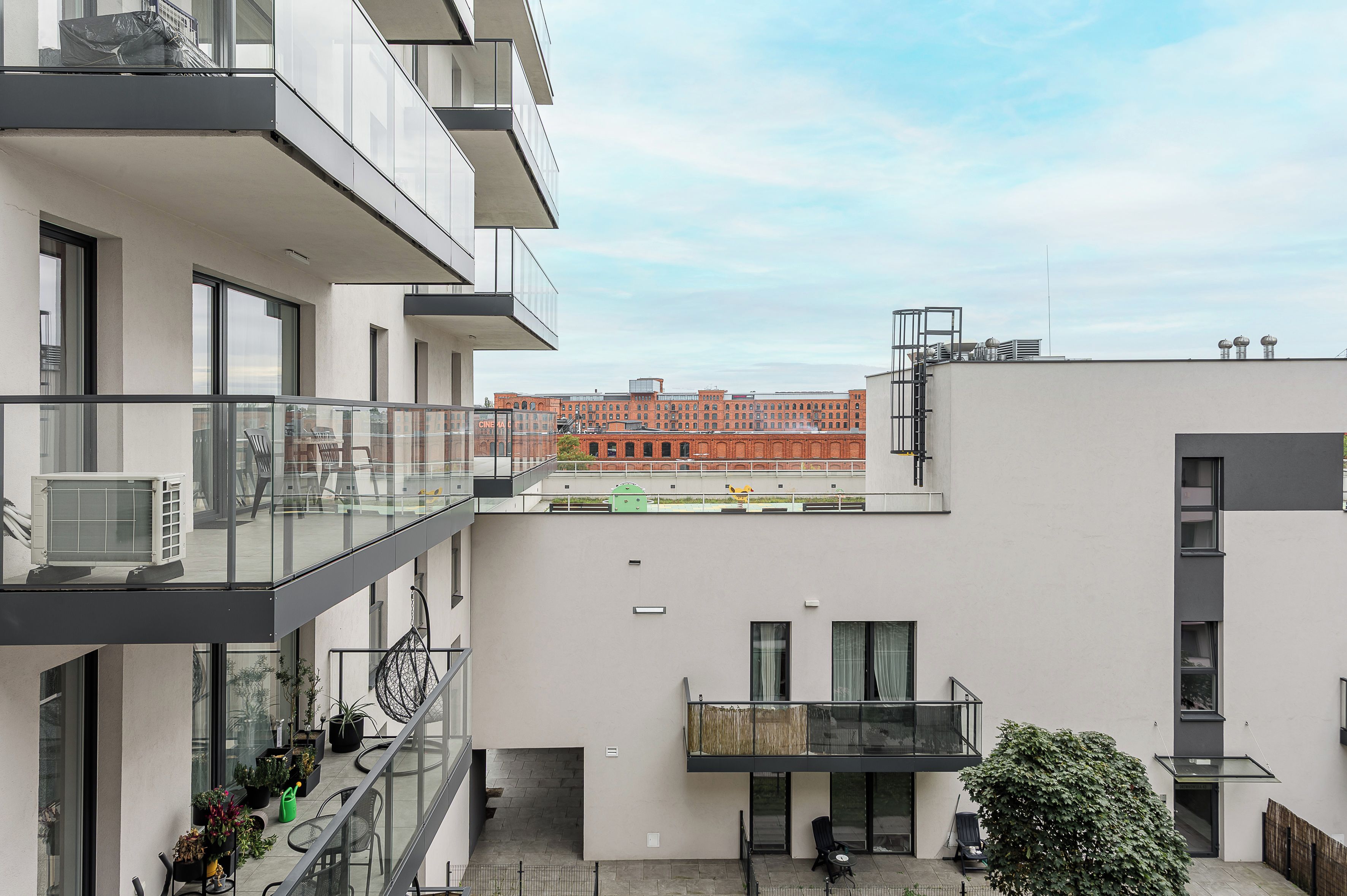 Un immeuble d’appartements moderne doté de balcons, d’une cour intérieure et offrant une vue sur un bâtiment historique en arrière-plan.