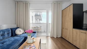 Una sala de estar moderna con un sofá azul, una mesa de centro con revistas y vistas a un balcón con zona de comedor.