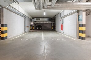 A multi-level underground parking garage with concrete floors and walls, marked parking spaces, and ventilation ducts. - Lumina 3room Apt w/ Parking  (Łódź)
