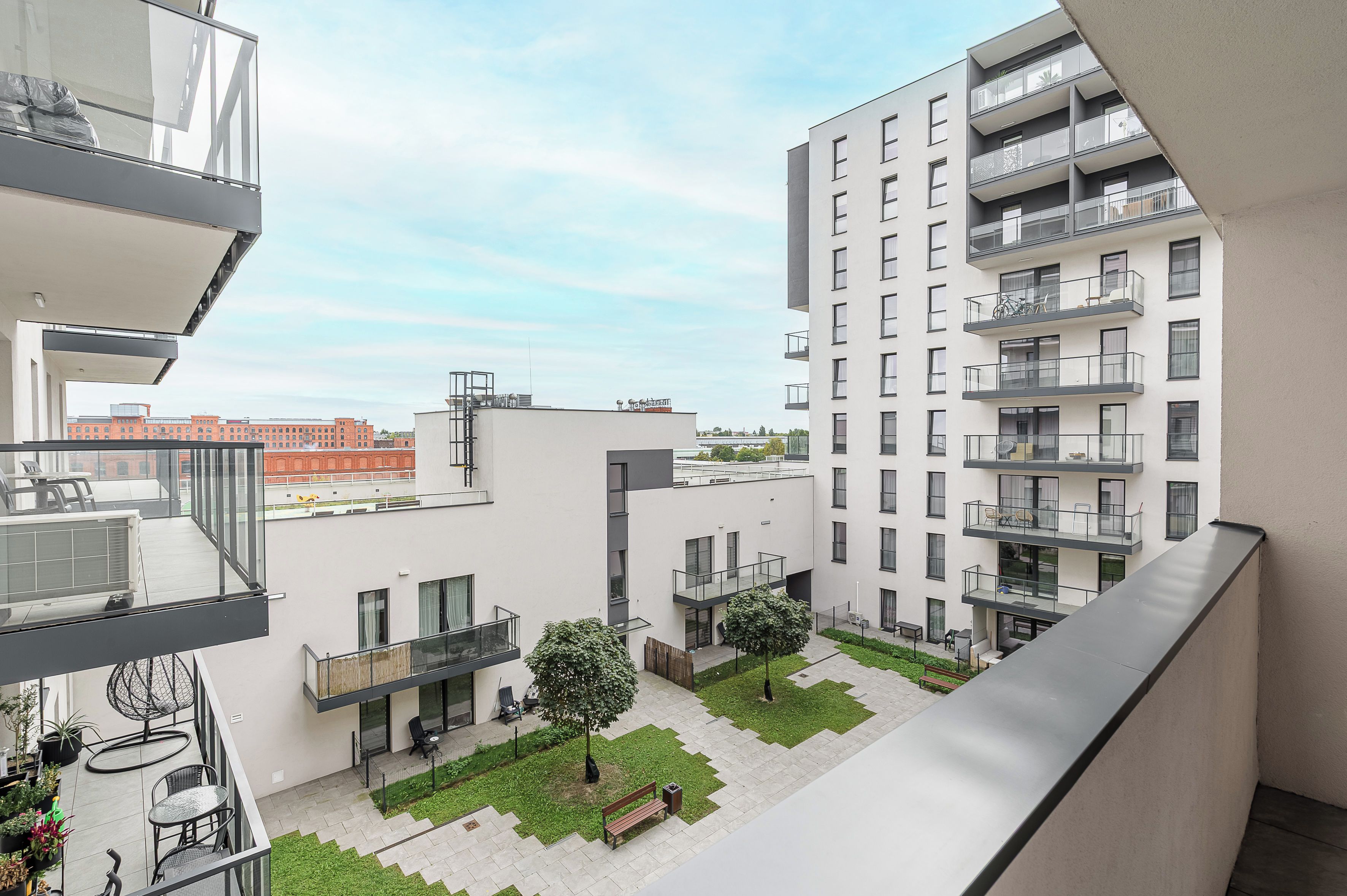 A modern apartment complex with balconies, a courtyard with seating, and a view of the cityscape.