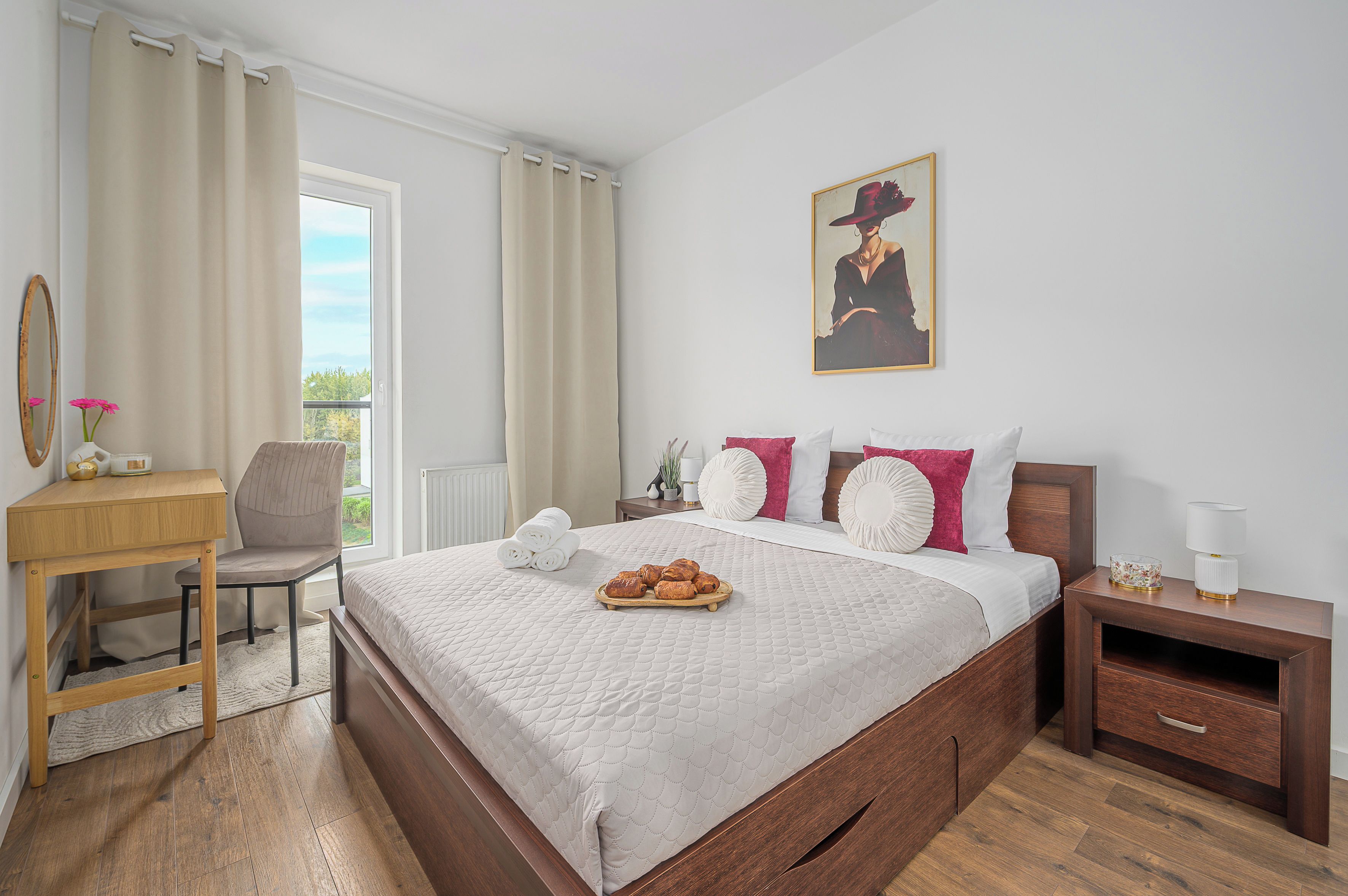 A hotel room with a wooden bed, a desk, a chair, a nightstand, and a painting on the wall.