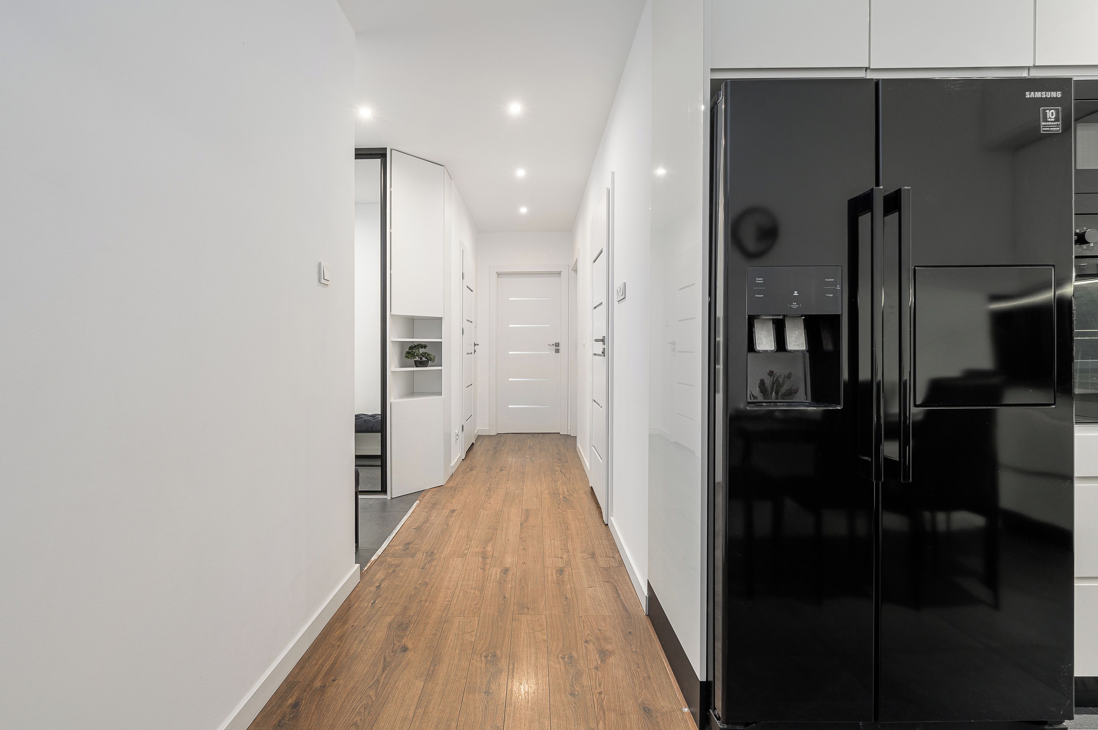 Una cucina moderna con frigorifero nero, mobili bianchi e pavimento in legno.