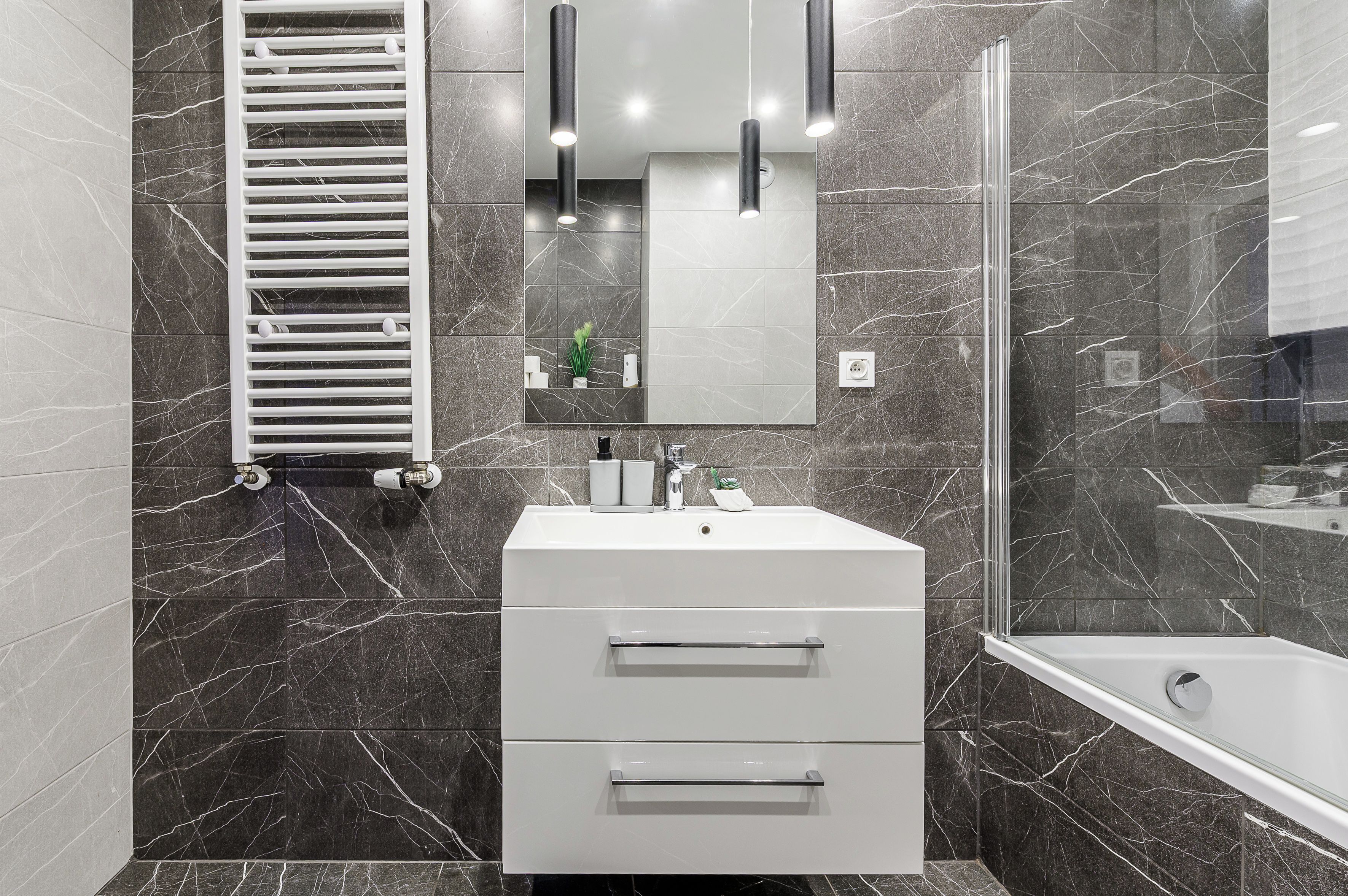 Een moderne badkamer met een wit aanrecht, een douchecabine van glas en een betegelde muur van marmer.