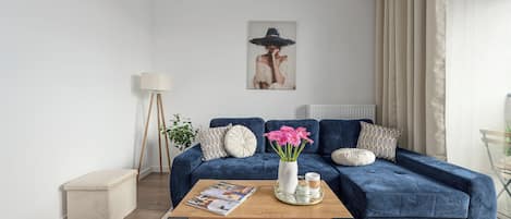 Una sala de estar con un sofá azul, una mesa de centro, un cuadro y una lámpara de pie.