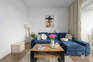 Una sala de estar con un sofá azul, una mesa de centro, un cuadro y una lámpara de pie.