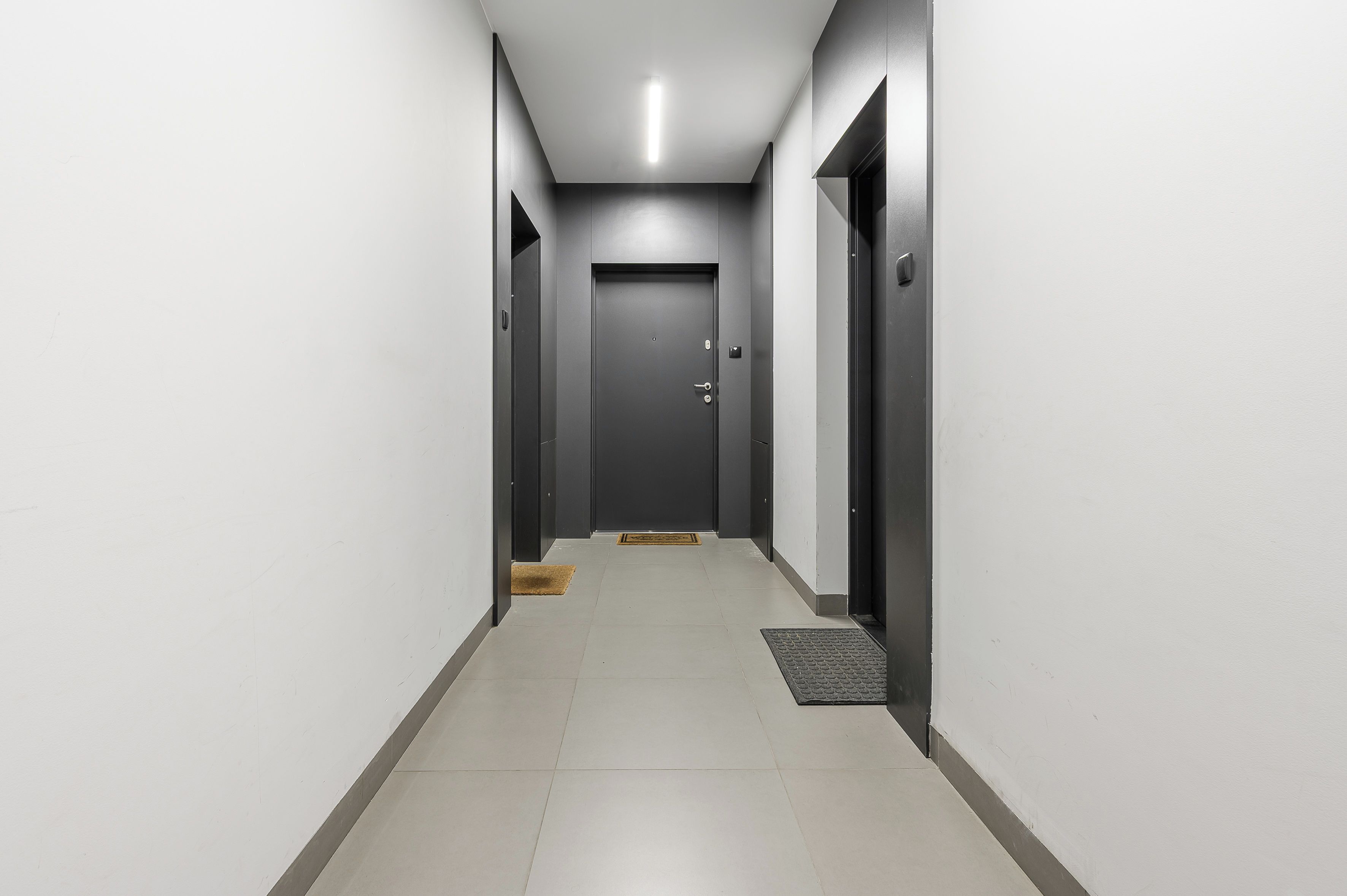 A corridor with doors on both sides, a doormat, and a mat at the entrance.