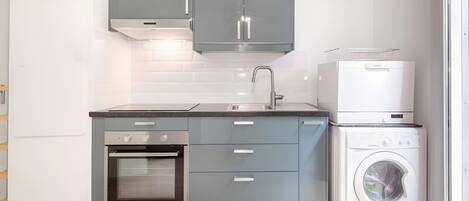 A compact kitchen with grey cabinets, a built-in oven, a sink, and a stacked washer and dryer.
