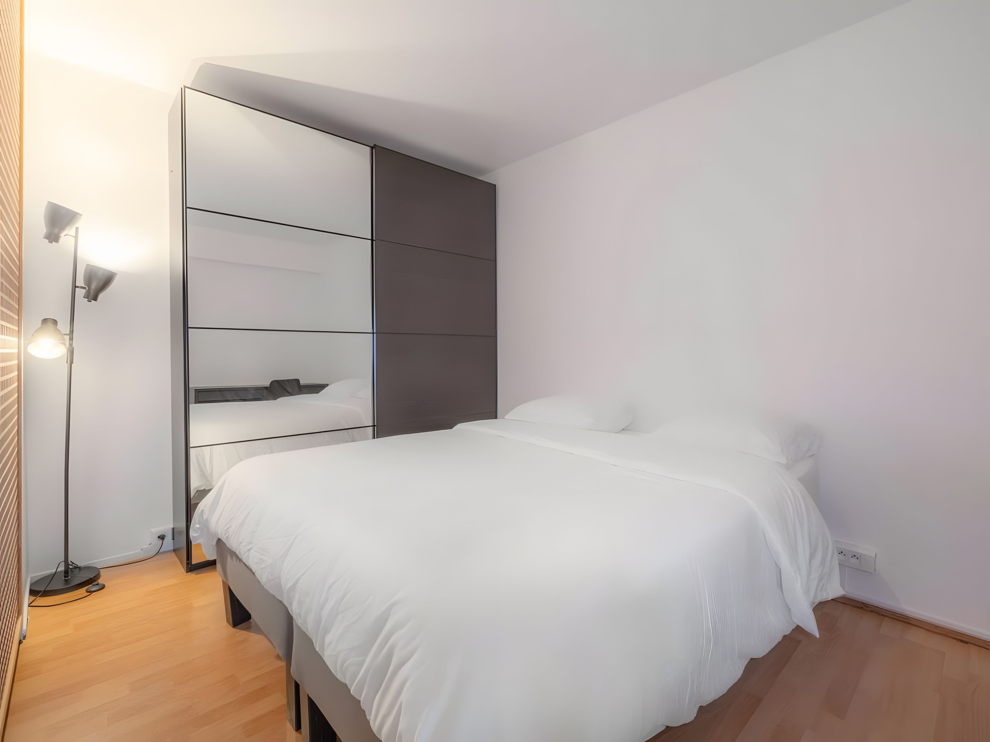 Een moderne slaapkamer met een bed, een kledingkast en een vloerlamp.