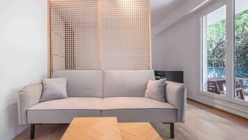 A modern living room with a sofa, a wooden coffee table, and a large window offering a view of the outdoors.