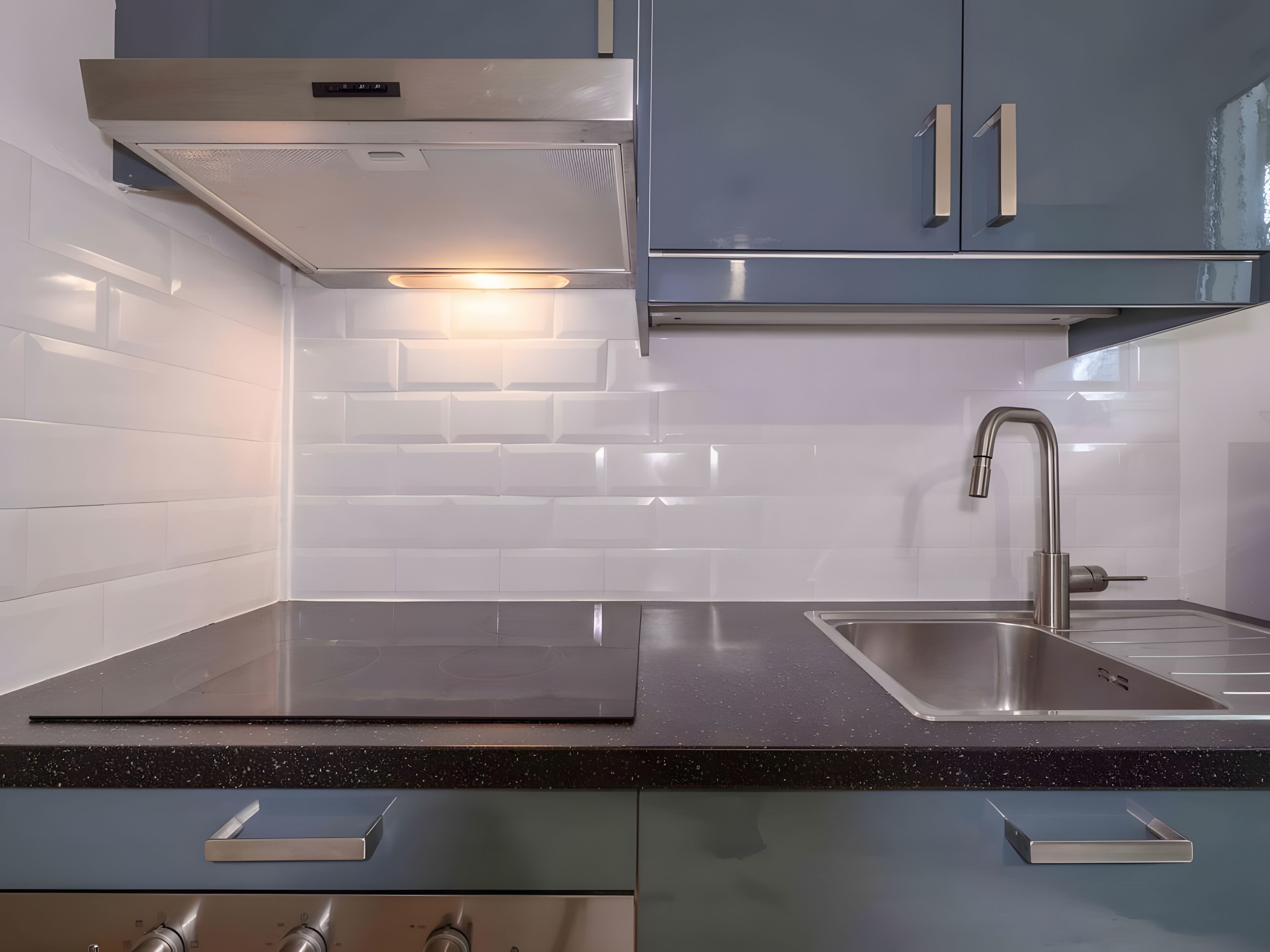 A modern kitchen with a stainless steel sink, a range hood, and a backsplash of white tiles.