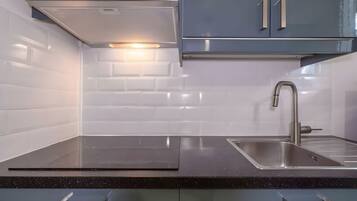 A modern kitchen with a stainless steel sink, a range hood, and a backsplash of white tiles.